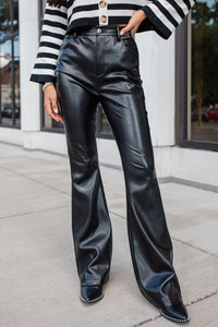 Person wearing black leather pants and a striped shirt on a sidewalk.