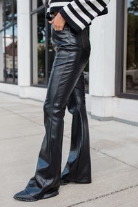 Person wearing black leather pants and a striped sweater on a sidewalk.