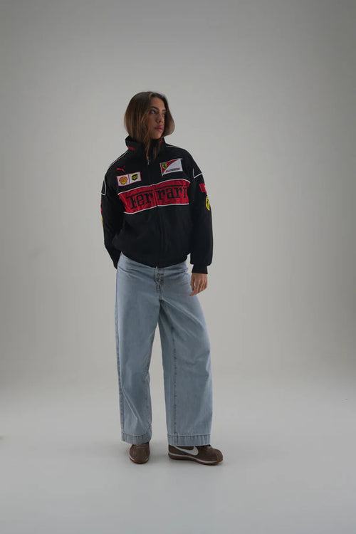 Person wearing a black ferrari jacket with colorful text and graphics on a plain background