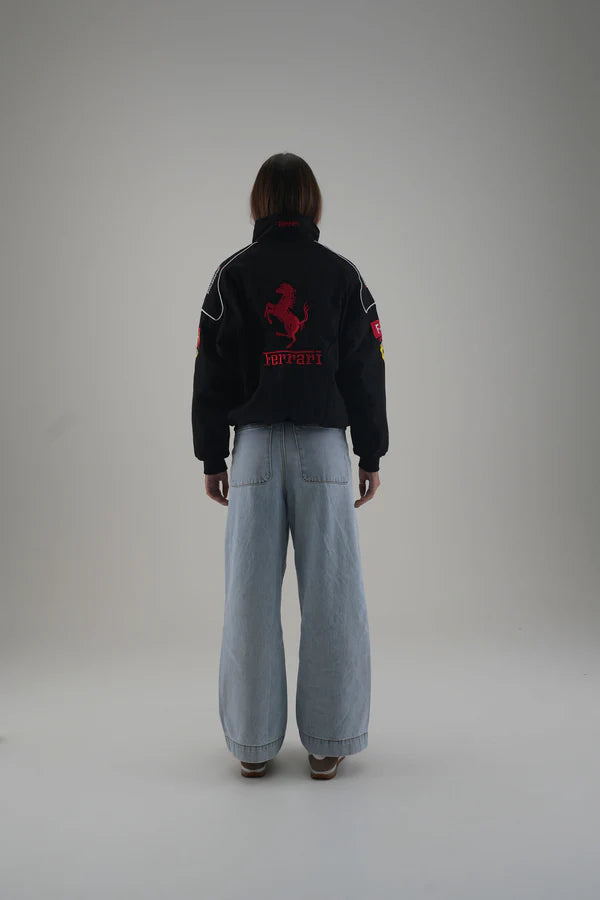 Person wearing a black ferrari jacket with a red logo and light blue pants on a gray background