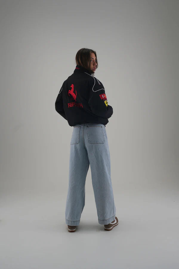 Person wearing a black jacket with logos and light blue jeans on a gray background
