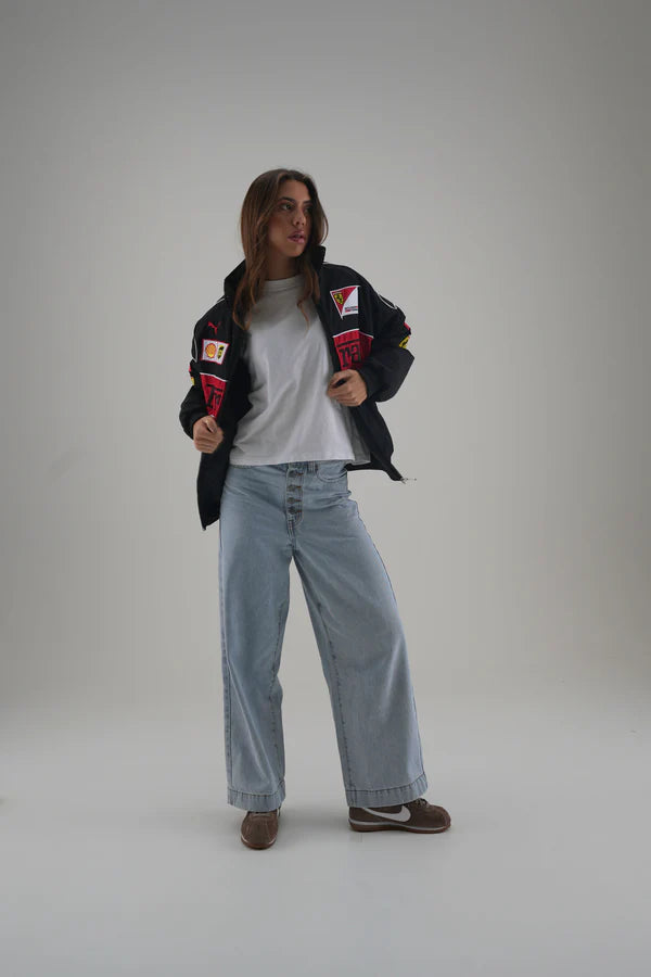 Person wearing a black ferrari jacket with patches, white shirt, and light blue jeans on a gray background