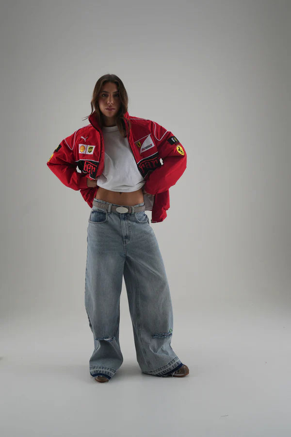 Person wearing a  red ferrari jacket with logos, white shirt, and blue jeans on a gray background