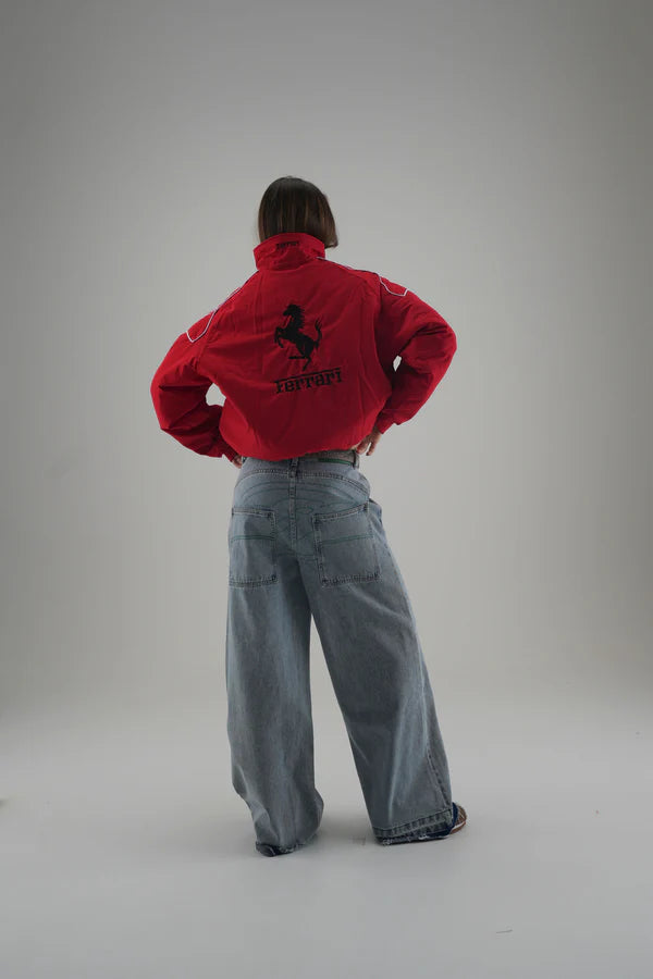 Person wearing a  red ferrari jacket with a logo on the back, standing against a plain background
