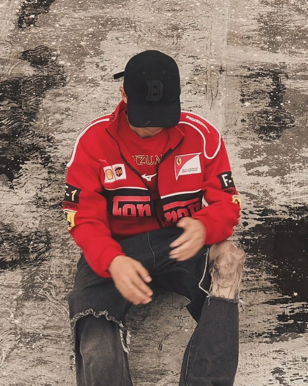 Person wearing a red jacket with various logos sitting against a textured wall.