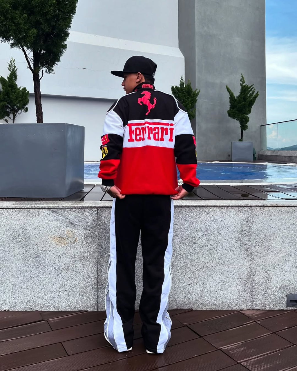 Person wearing a Ferrari tracksuit standing outdoors with a building and trees in the background