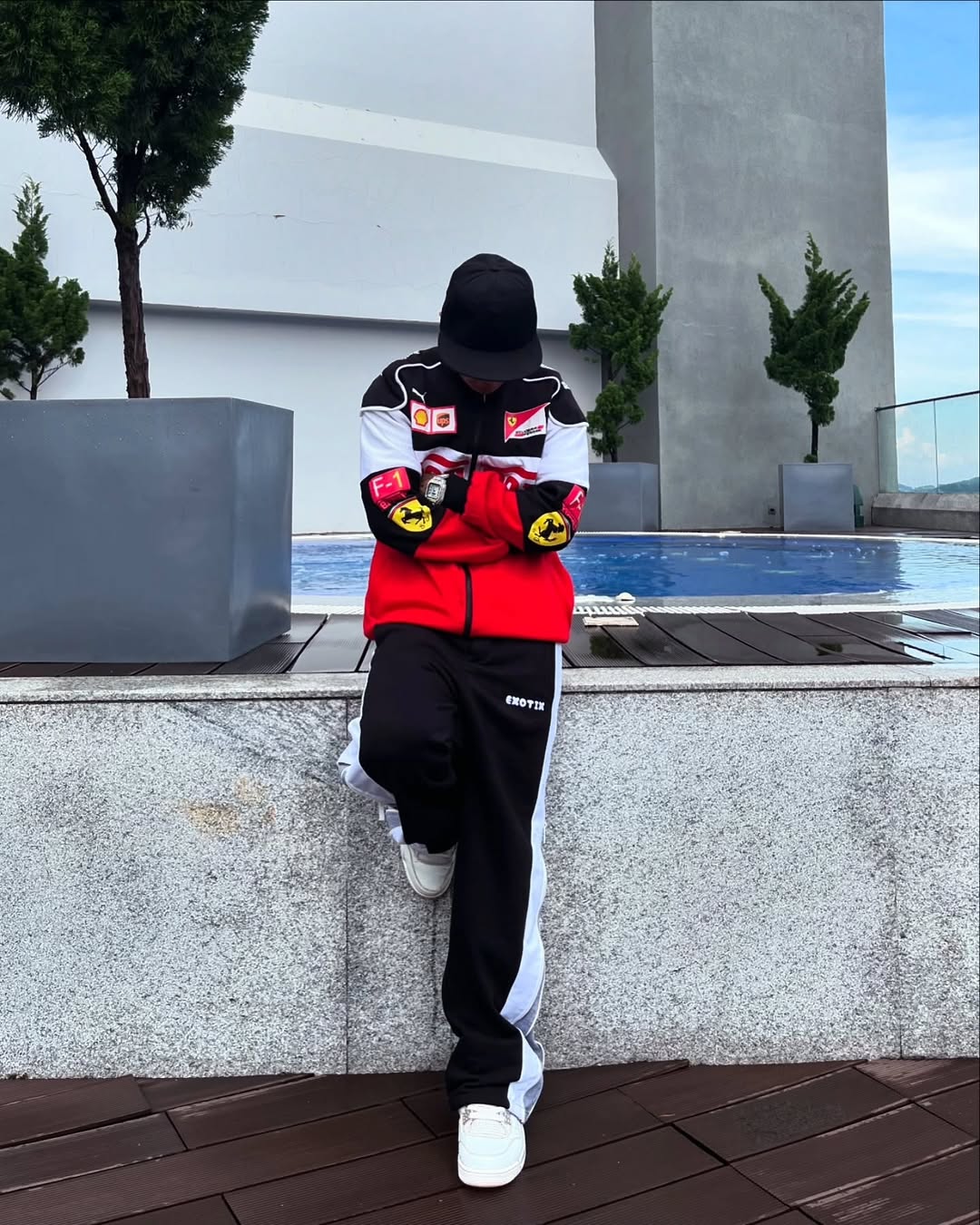 Person wearing a black and red outfit with a hood, standing by a poolside.