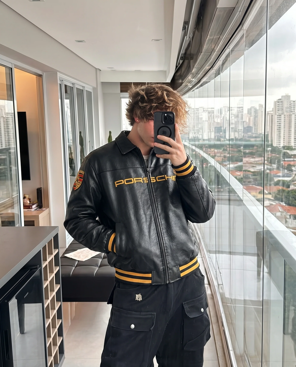 Front view of the unisex Black Porsche Leather Jacket on a male model, highlighting the high-density embroidered motorsport patches and heavy-duty front zipper.