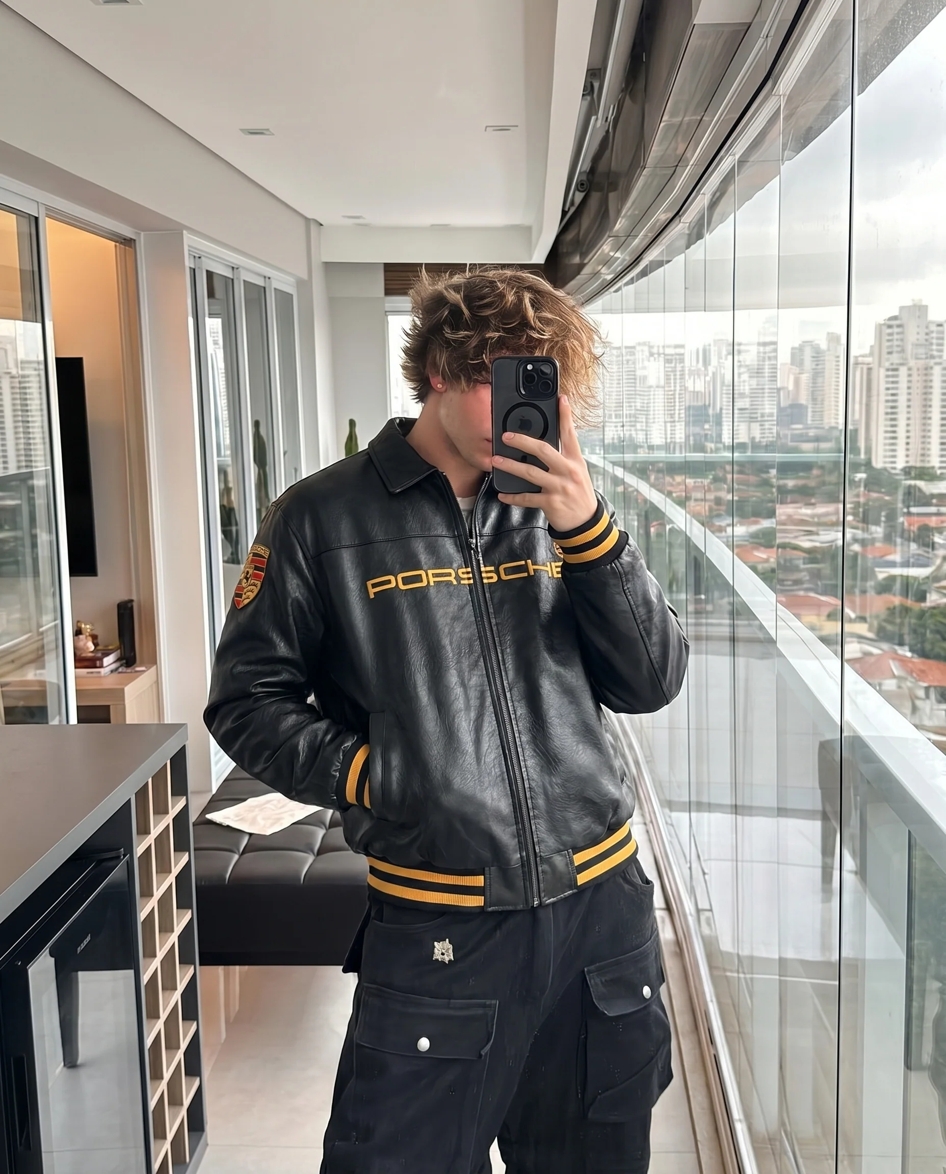 Front view of the unisex Black Porsche Leather Jacket on a male model, highlighting the high-density embroidered motorsport patches and heavy-duty front zipper.