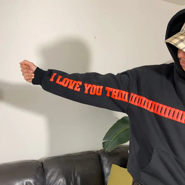 Person wearing a black hoodie with orange text 'I LOVE YOU THIS' in a casual setting.