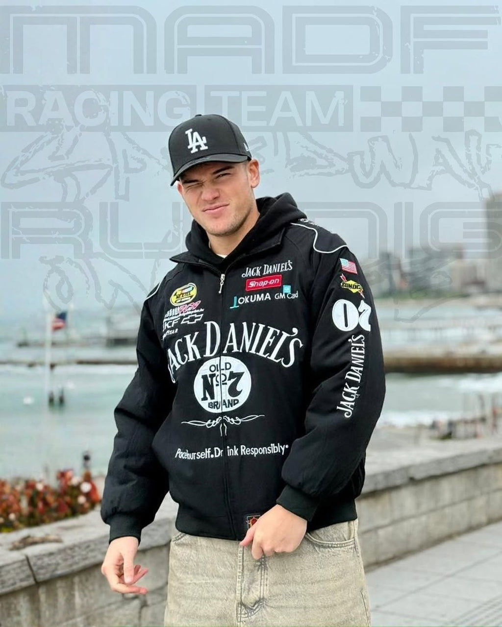 Person wearing a jack daniel jacket with various brand logos by a waterfront.