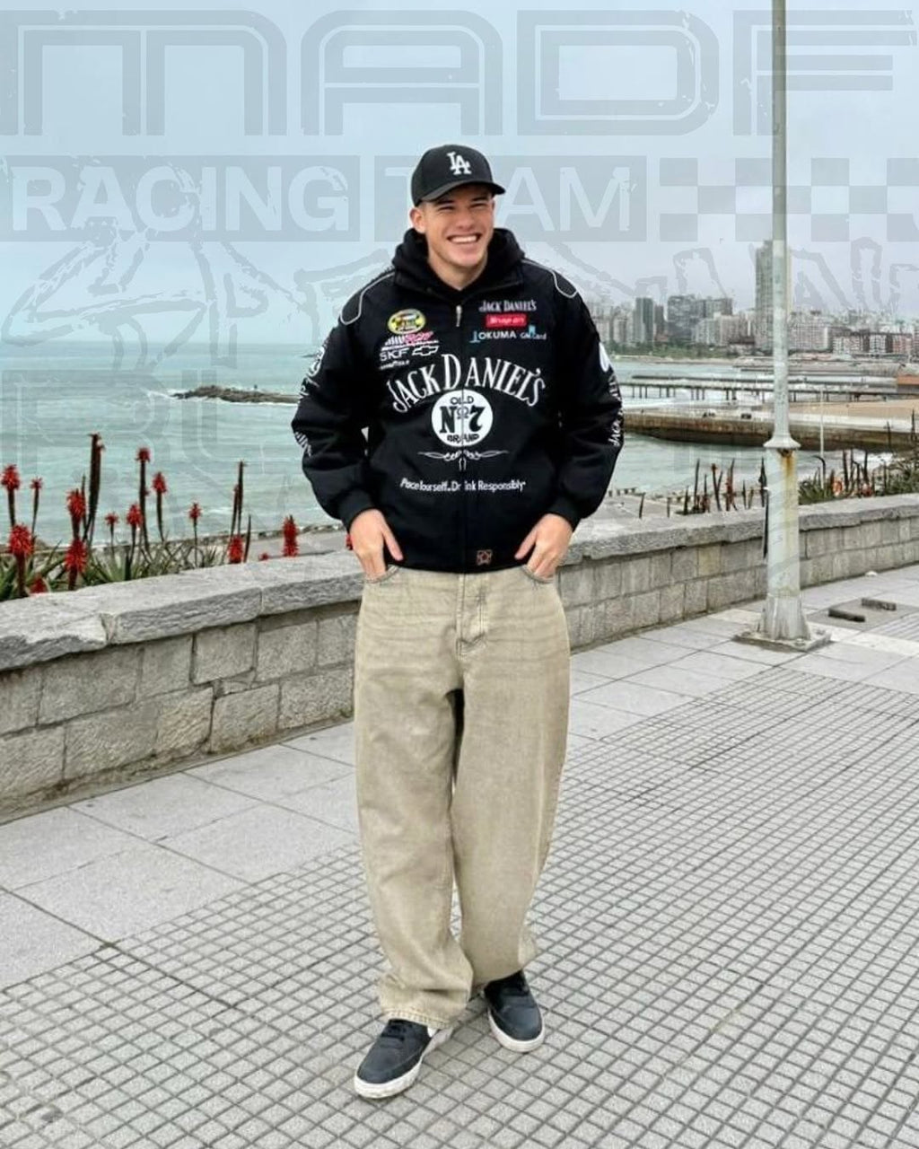 Person wearing a jack daniels jacket and pants standing by a waterfront with 'Racing Team' text in the background.