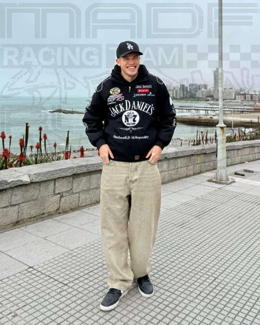 Person wearing a jack daniels jacket and pants standing by a waterfront with 'Racing Team' text in the background.