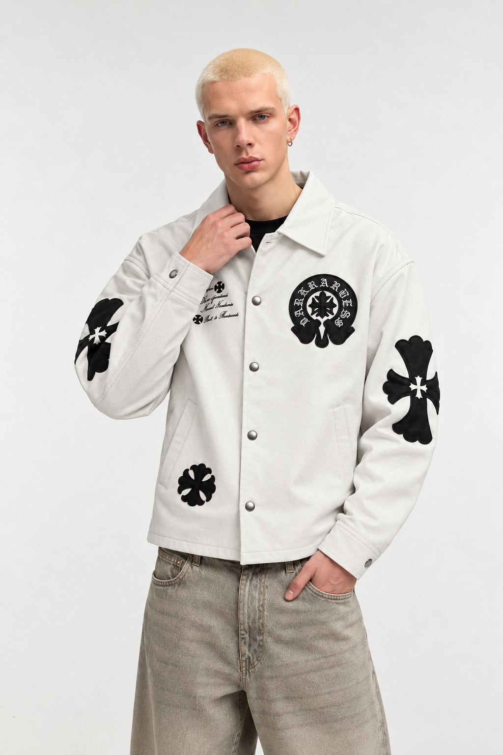 Male model wearing the cream Gothic cross trucker jacket unsnapped over a basic tee, showing the smooth interior polyester lining