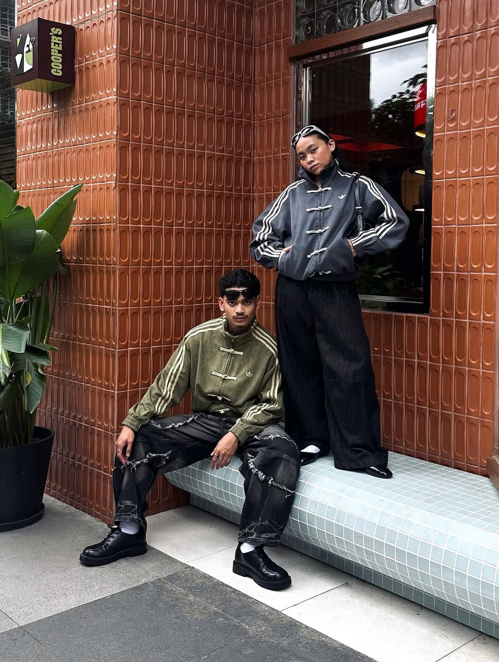 Profile view of the couple wearing Streetbred CNY earth-tone jackets. The extreme dropped shoulder geometry perfectly perfectly illustrates how the boxy cut functions seamlessly as high-end mens and womens streetwear.