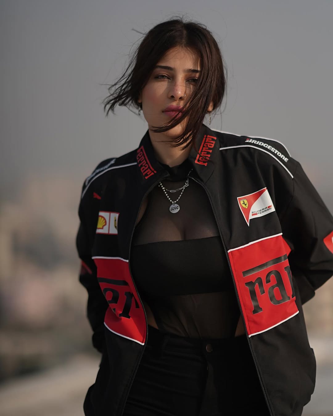 Front view of a female model wearing the unisex Streetbred Black Ferrari F1 Jacket with baggy streetwear pants.