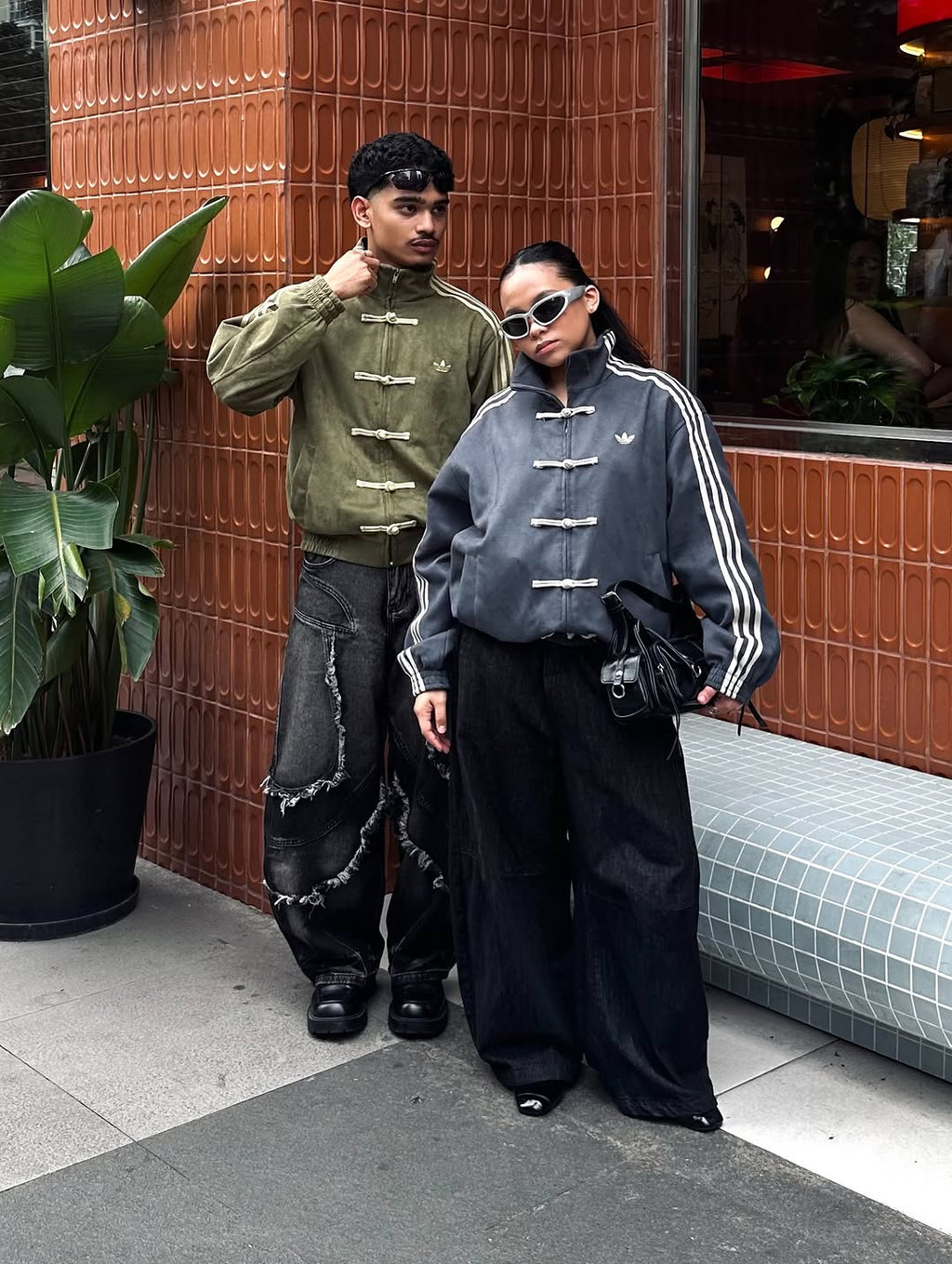 Full body shot of a male and female model wearing the matching Oversized CNY Knot Jackets in Olive Green and Dark Grey. Showcases the perfect unisex streetwear drape and genderless darkwear aesthetic for couples in India.